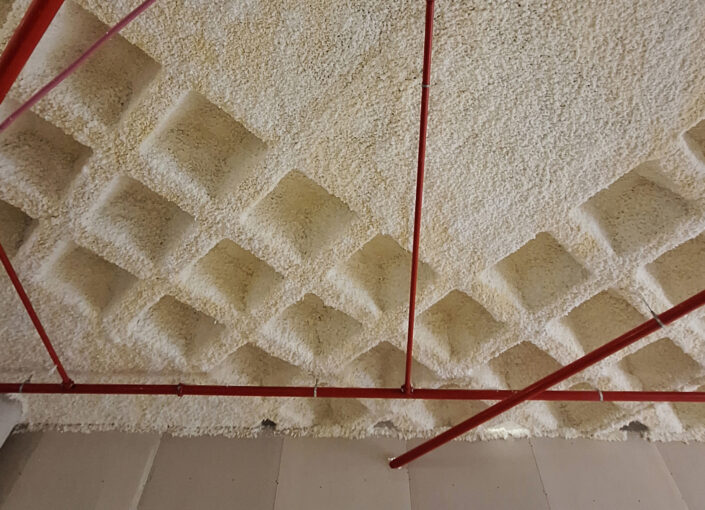 Detalle de techo ignifugado con mortero de lana de roca proyectado como protección pasiva contra incendios en una estructura de edificación.